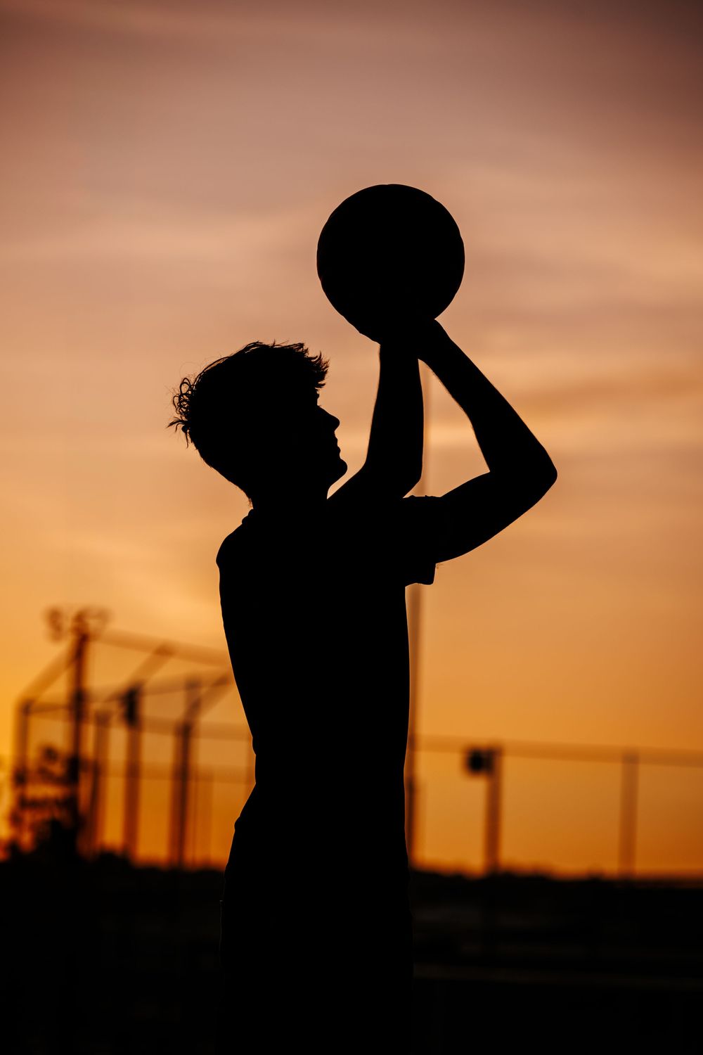 Silhouette of basketball player shooting against dramatic sunset sky.