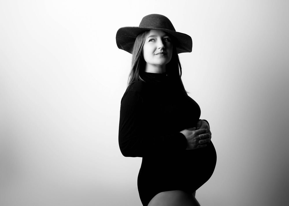 Black and white studio portrait of someone in a wide-brimmed hat and turtleneck posing against light backdrop.