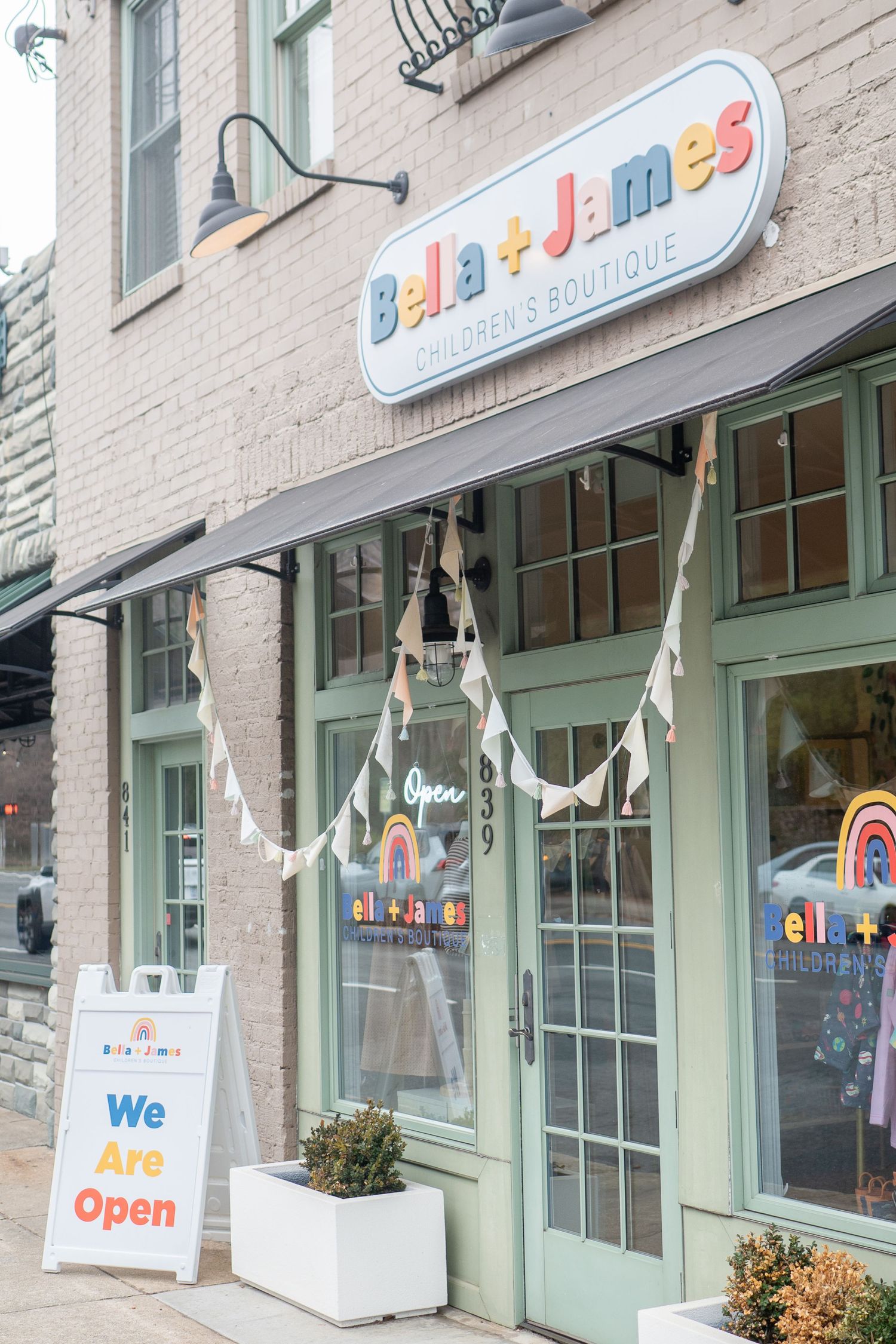 Storefront of Bella James boutique with mint green doors and colorful signage on a beige brick building.
