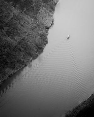 Aerial view of a calm river bend surrounded by steep forested slopes in black and white.