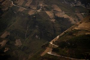 Birds-eye view of winding mountain roads cutting through terraced agricultural landscape.