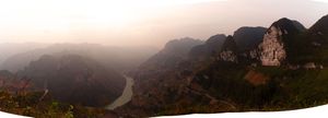 Panoramic mountain landscape with dramatic peaks and valleys shrouded in misty clouds during sunset.