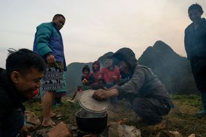 Group gathered around a campfire in the mountains at dusk with camping gear visible.