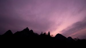 Purple and pink sunset sky panorama with dramatic cloud formations over mountain silhouettes.