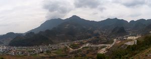 Wide panoramic view of mountain ranges under cloudy skies with rolling hills in foreground.