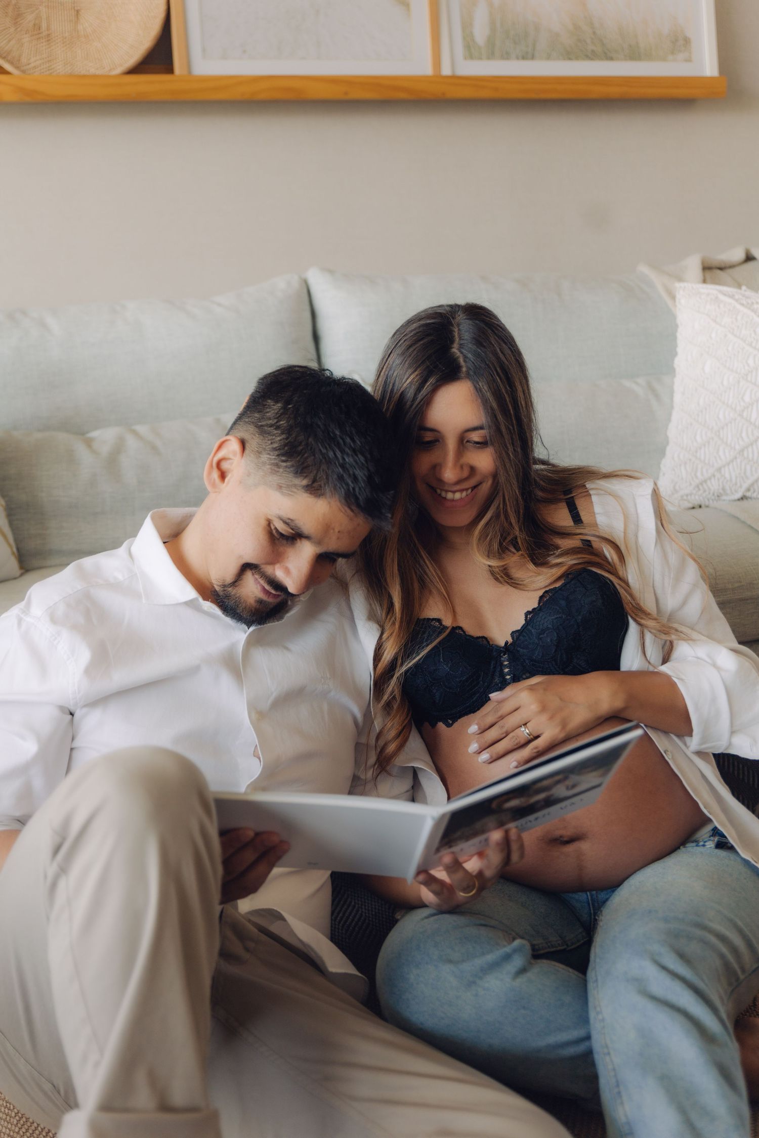 Expecting couple smiling while reviewing ultrasound photos together on living room couch.