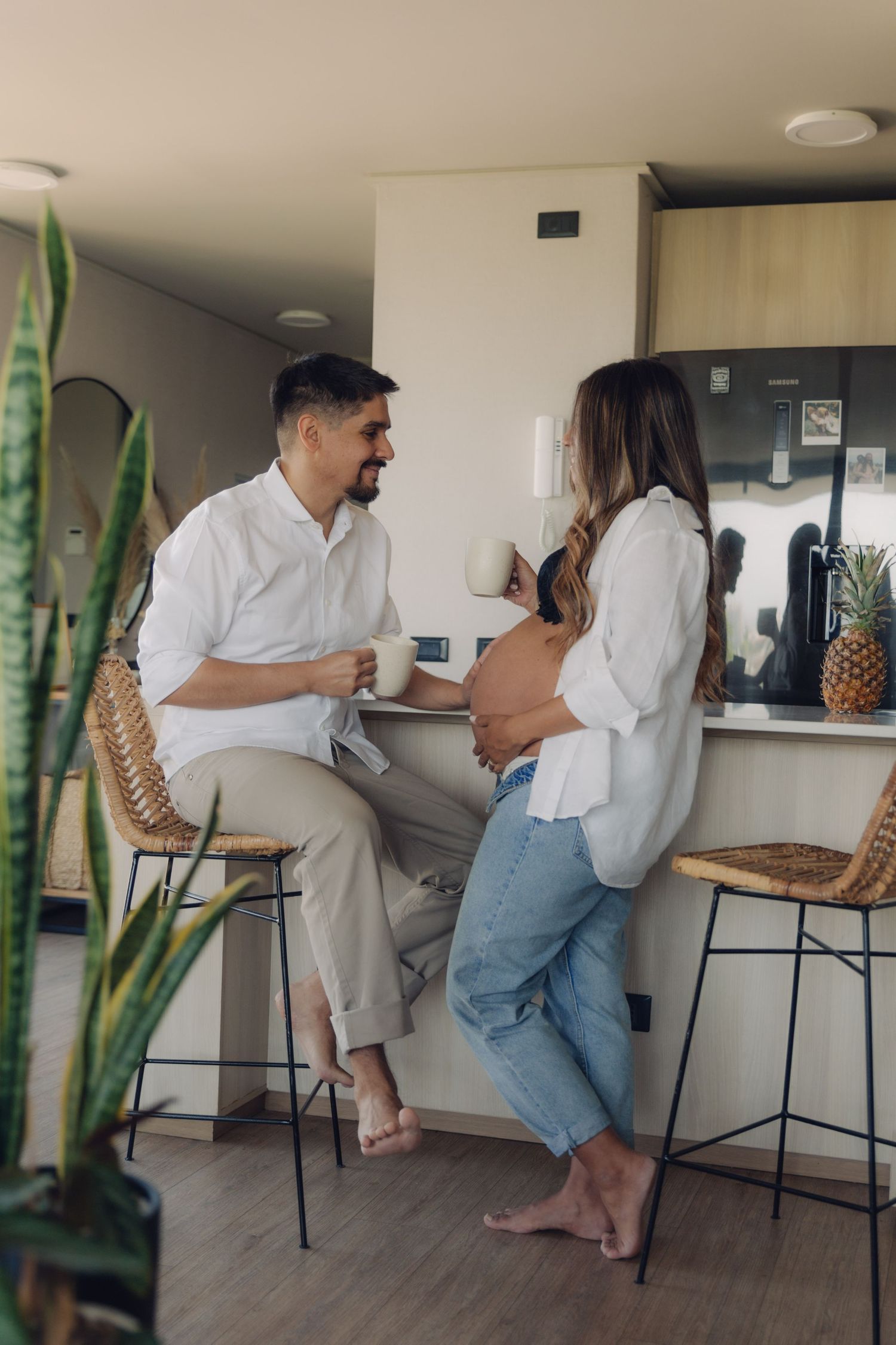 Happy expectant couple chatting over coffee in a bright modern kitchen with rattan bar stools.