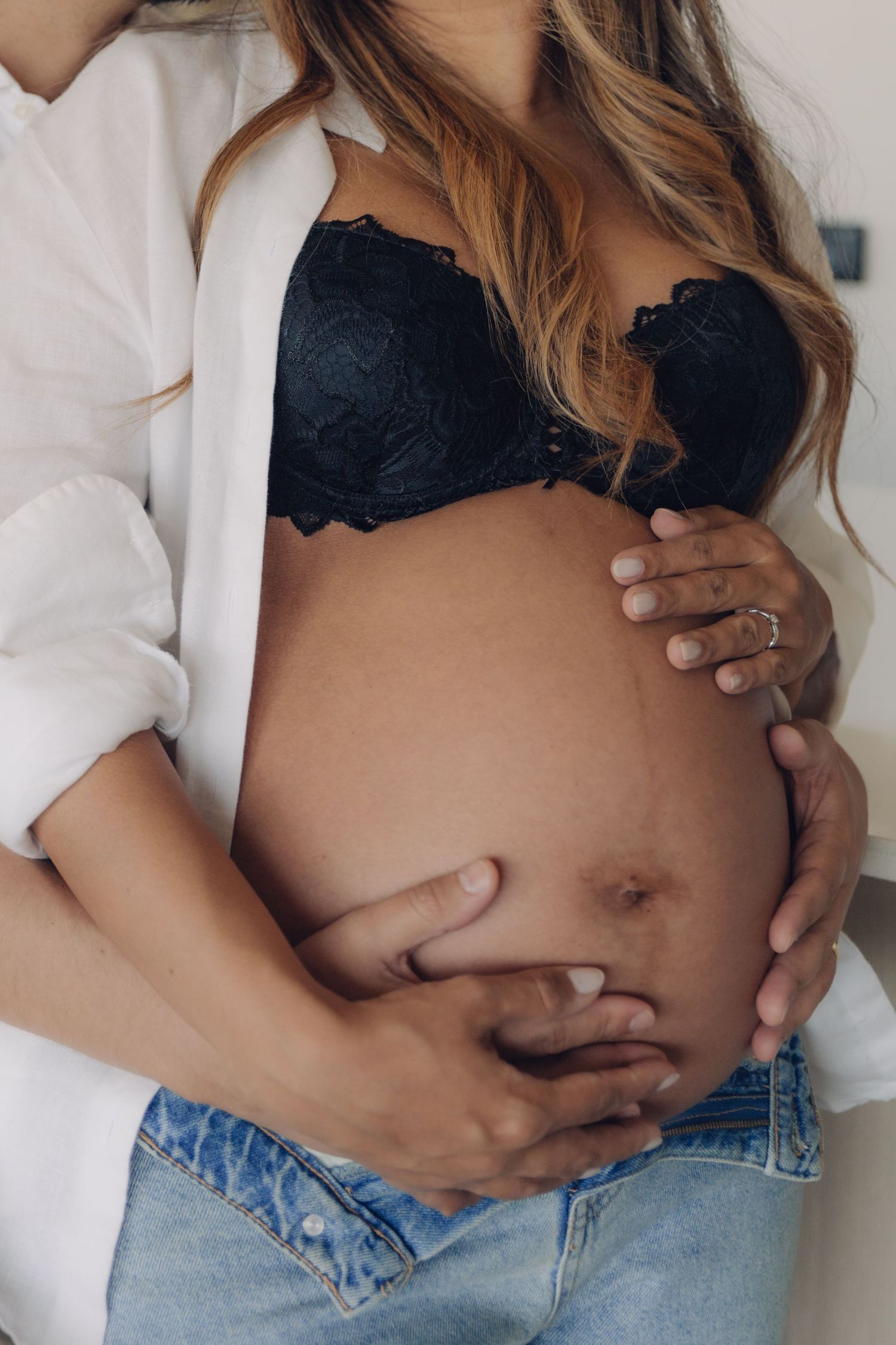 Close-up of pregnant woman's bare belly being tenderly held by both her and her partner's hands.