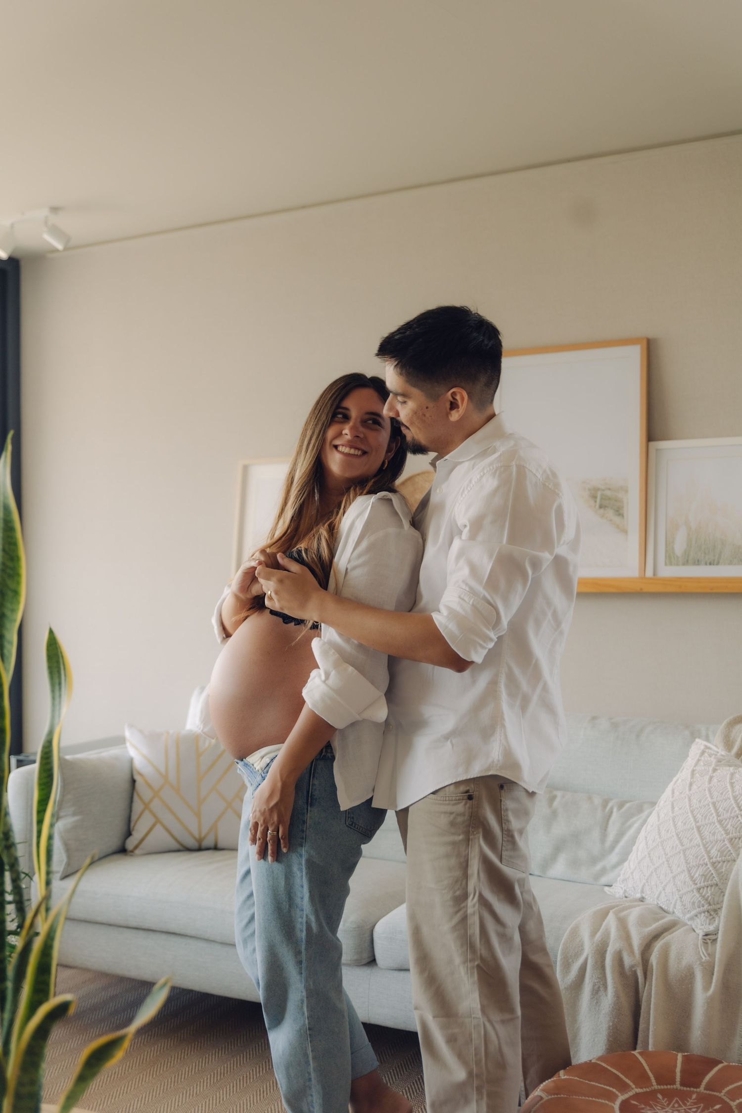 Loving couple embracing in modern living room, pregnant woman smiling as partner holds her close.