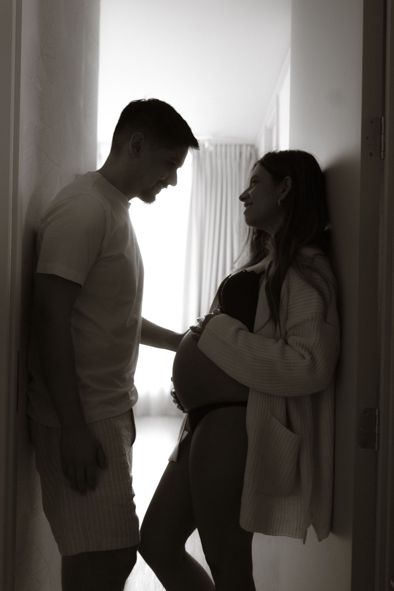 Black and white silhouette of expecting couple sharing tender moment in doorway, touching baby bump.