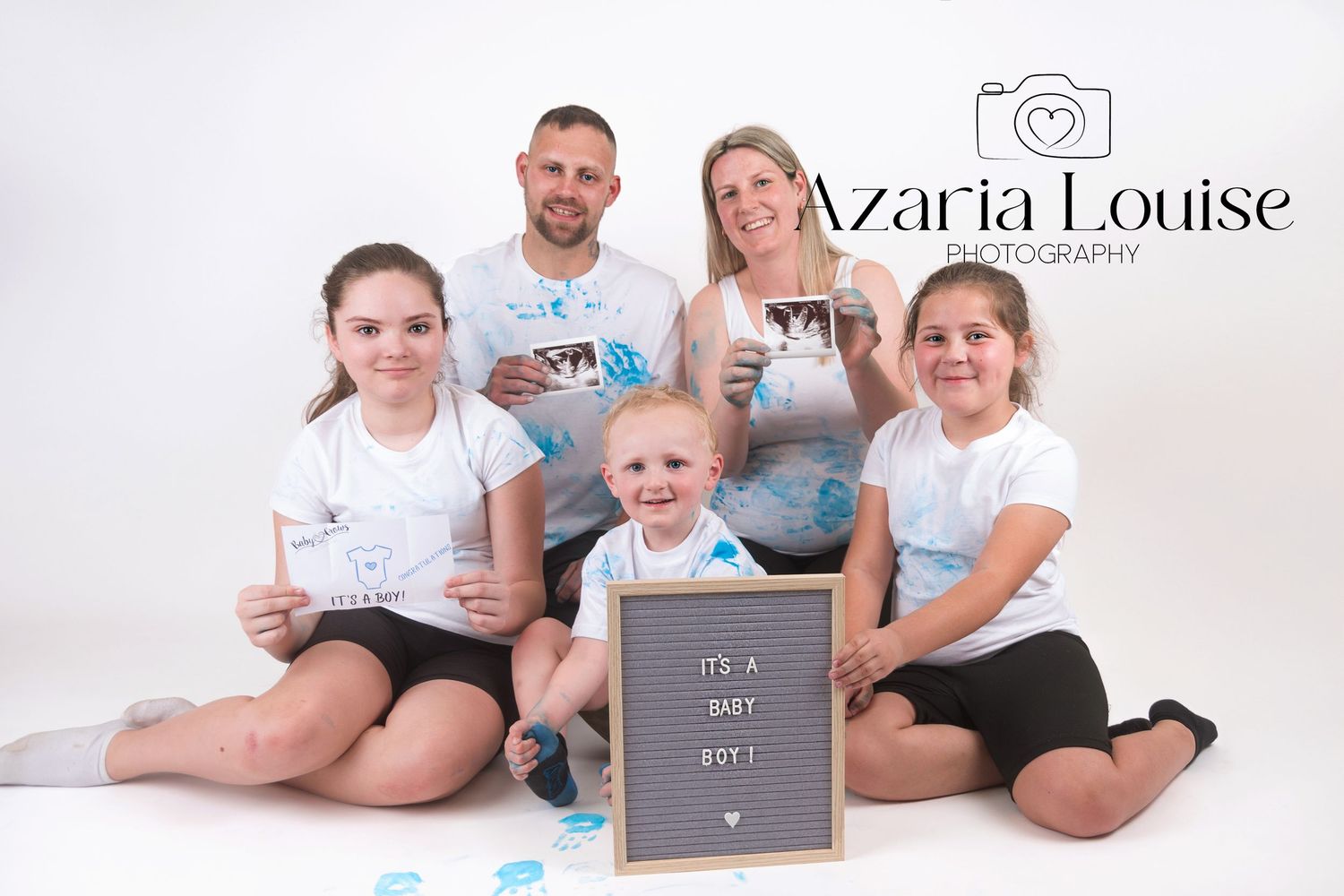A family poses together on a white background with a letterboard sign while wearing casual clothing.