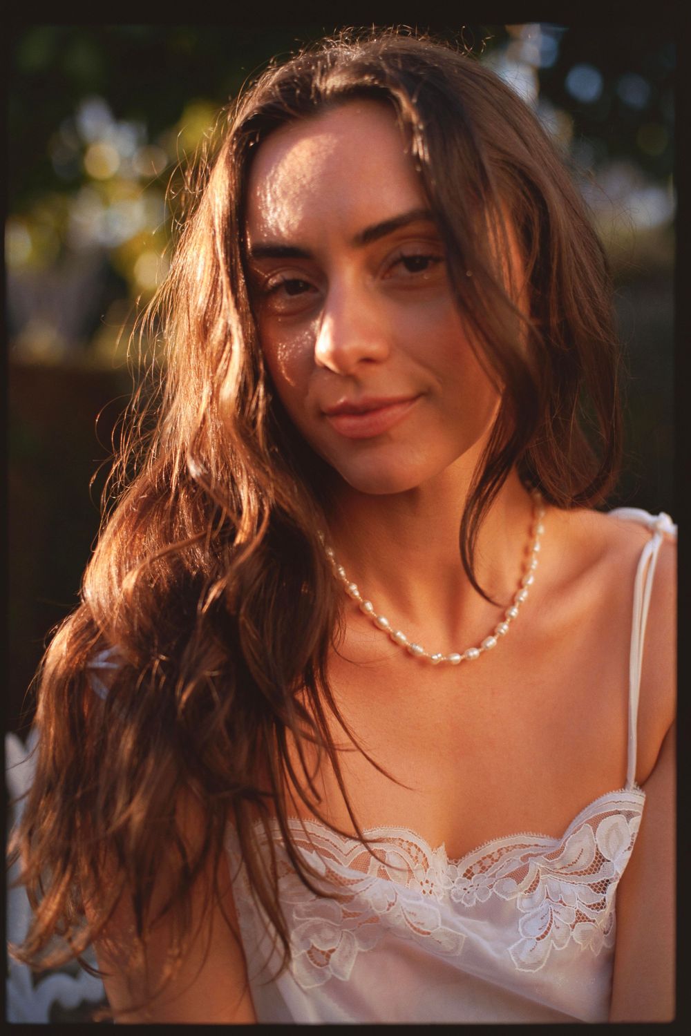 Close-up portrait of a woman with long wavy hair wearing pearls and white lace dress.