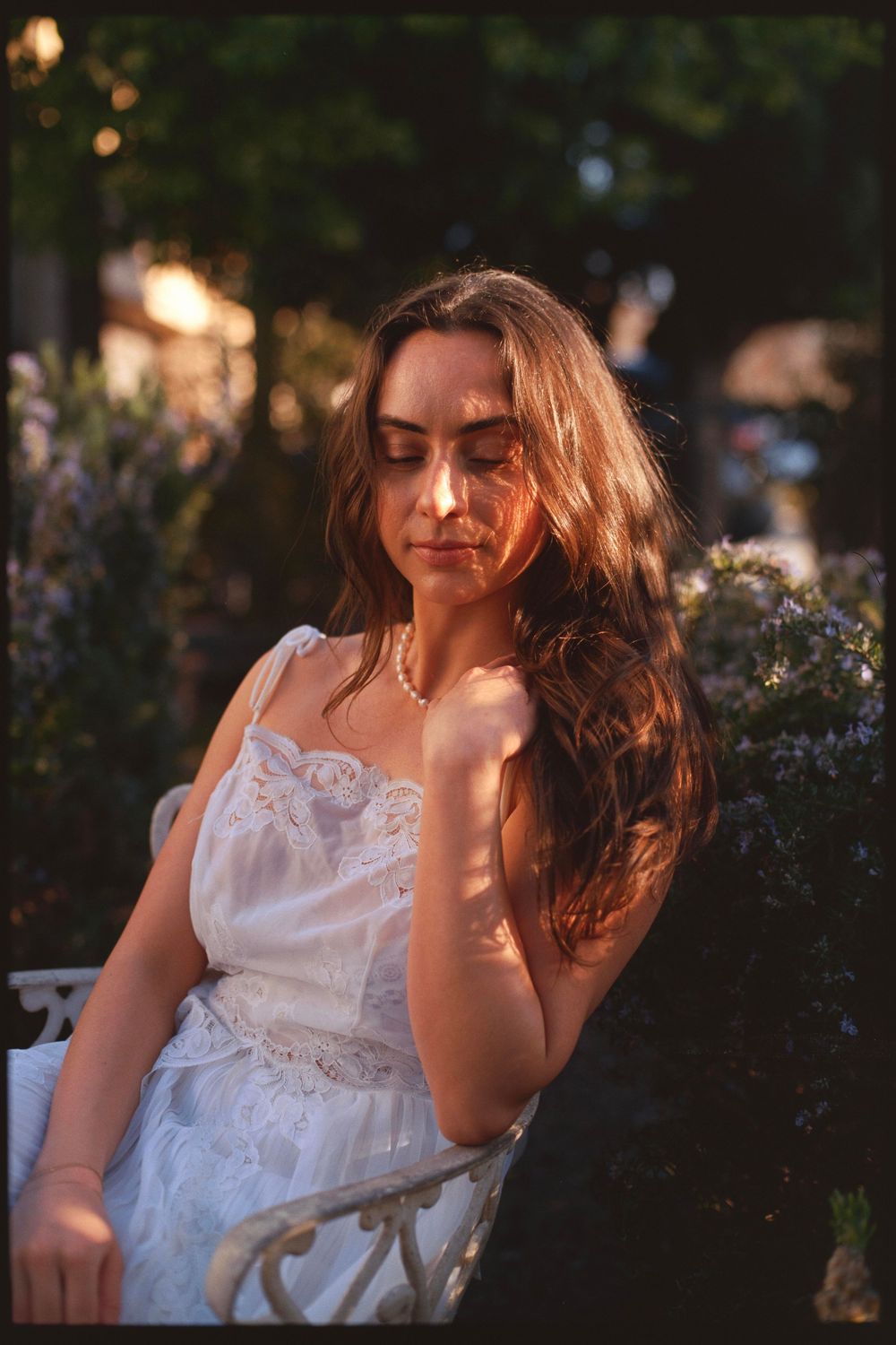 Soft sunlight creates dramatic shadows across white lace dress in garden setting.