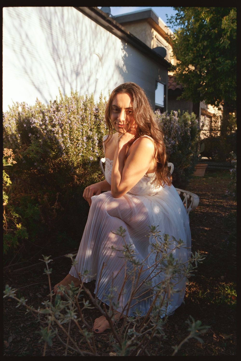 White dress against garden foliage in warm sunset lighting creates dreamy ethereal mood.