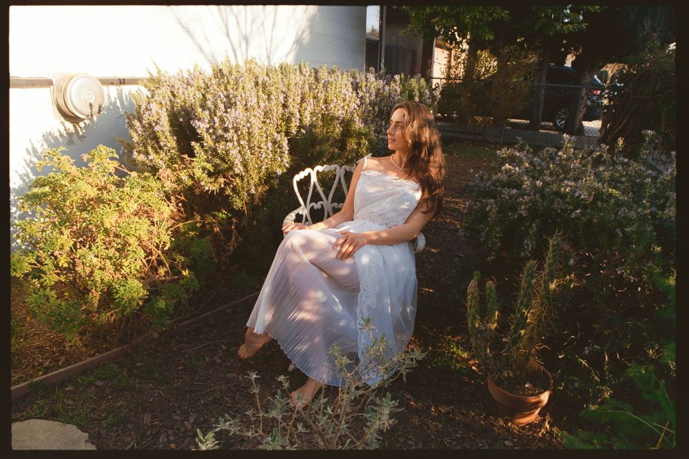 Flowing white dress contrasts with lush garden greenery in golden hour light.