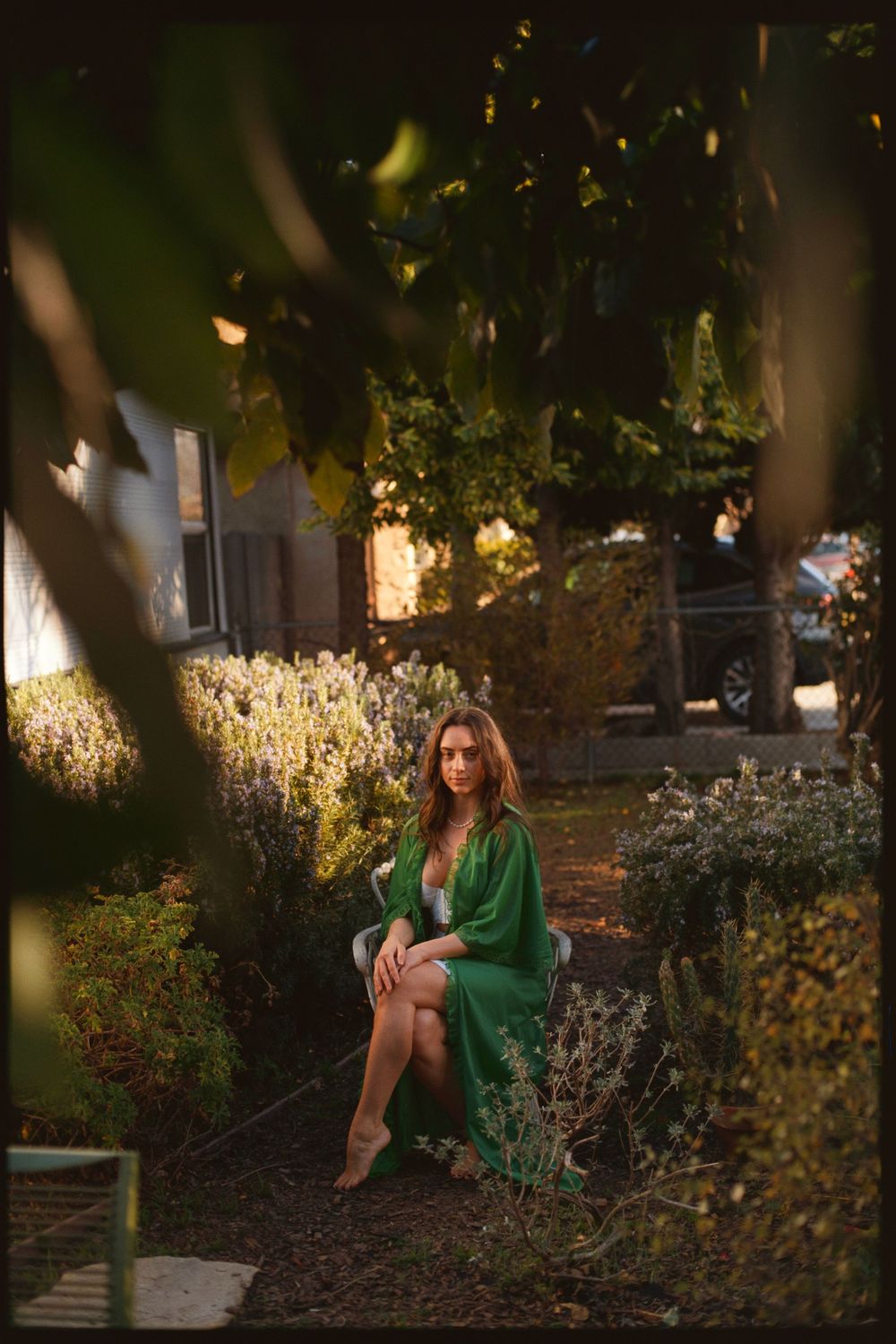Woman in green dress sitting in garden with dappled evening light.