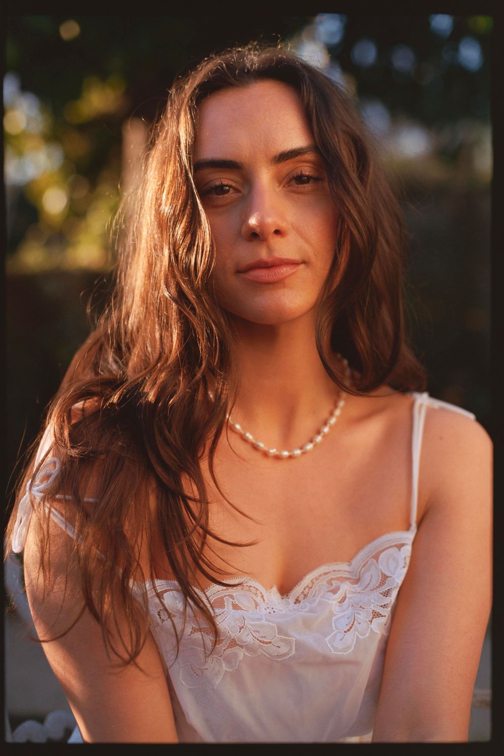 Portrait of a woman wearing pearl necklace and white lace top in golden hour lighting.