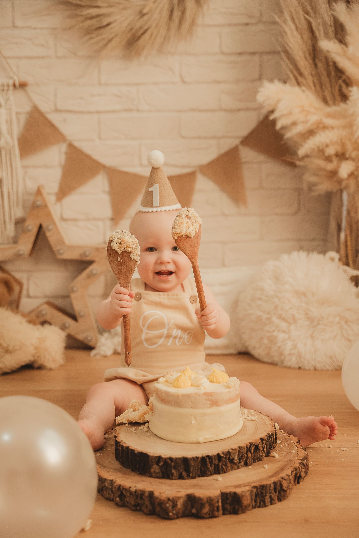 Rustic first birthday cake smash photo setup with pampas grass, wooden accents, and neutral tones on wood slice cake stand.