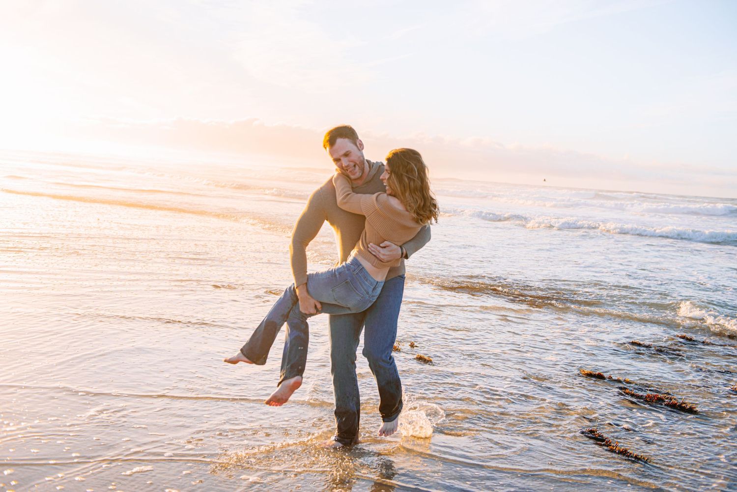 A couple plays in the shallow ocean water during sunset while enjoying a romantic moment at the beach in Monerey.