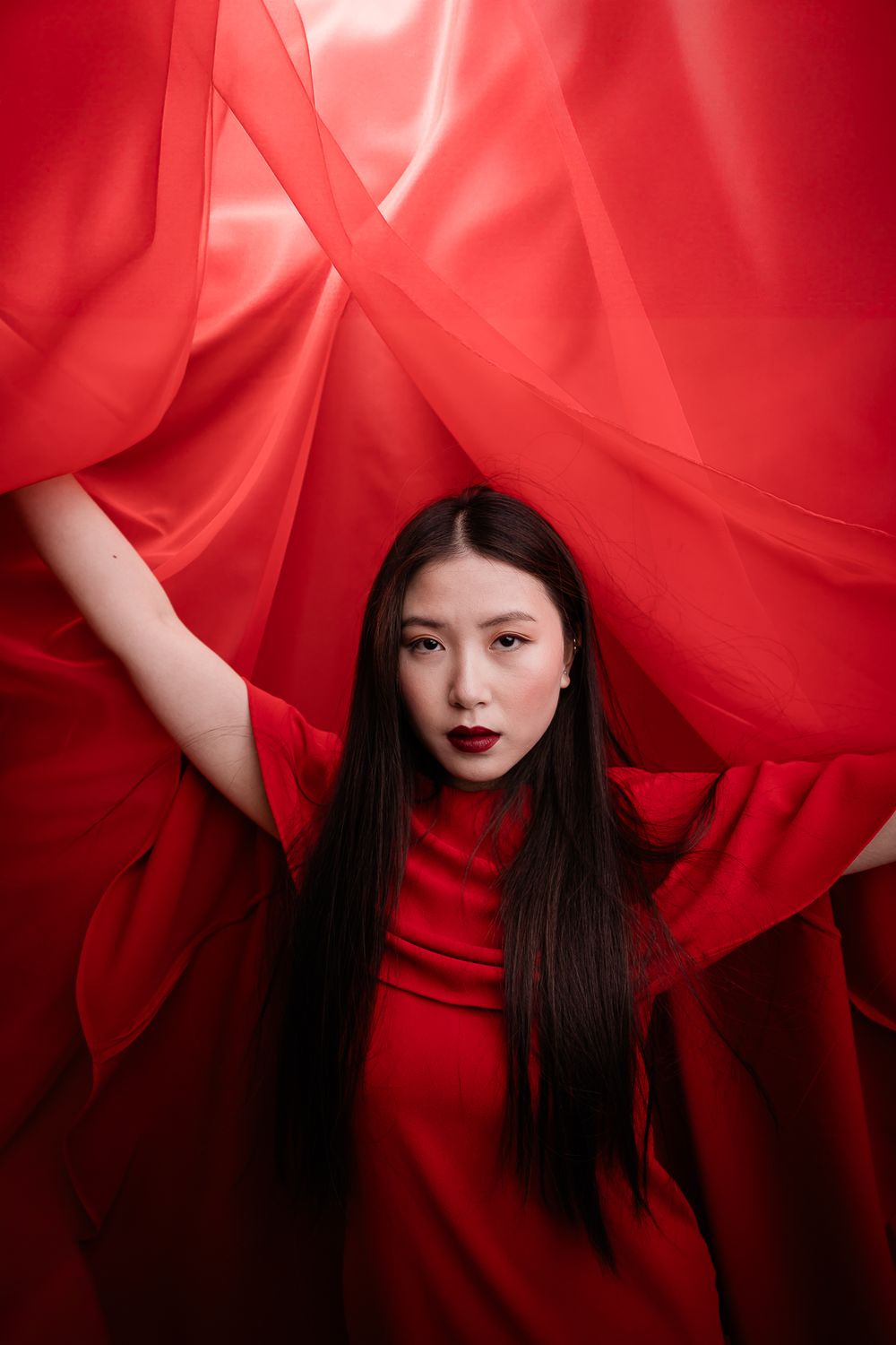 Dramatic fashion portrait with flowing red fabric and striking monochromatic styling.