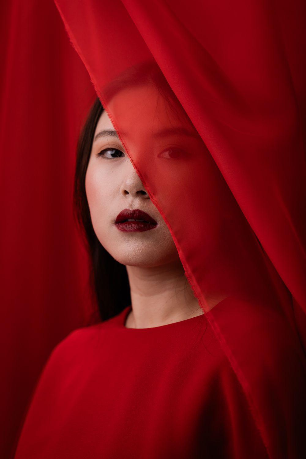 Artistic portrait with a red veil and matching dress against vibrant crimson background creates dramatic visual impact.