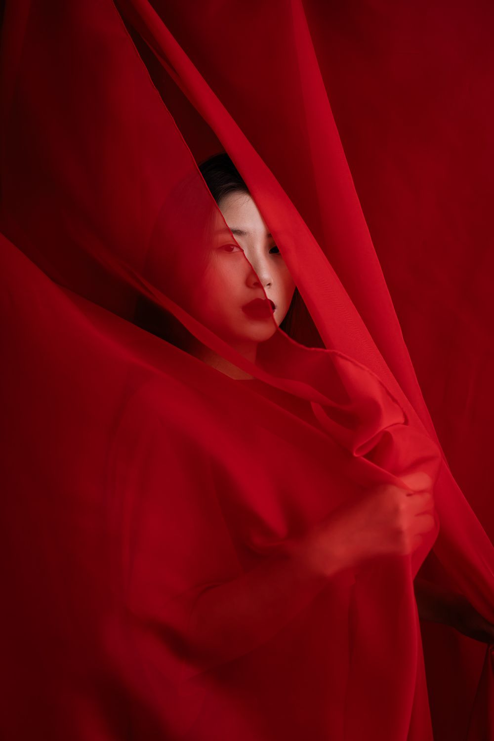 Artistic portrait silhouetted through flowing red fabric creating a dramatic and ethereal effect.