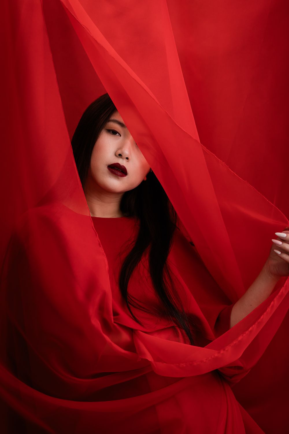 Artistic portrait draped in flowing red fabric against red background creating dramatic monochromatic effect.
