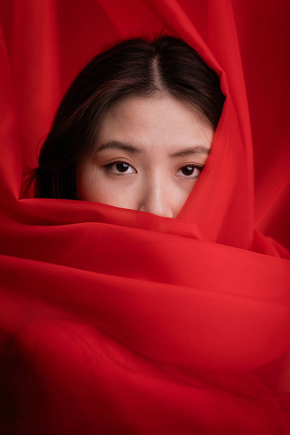 Artistic portrait with vibrant red fabric draping around figure against deep red background.