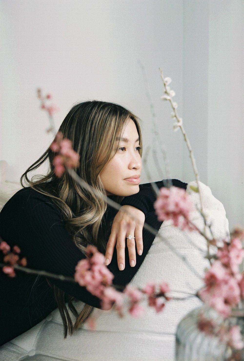 Person in black sweater gazing thoughtfully near cherry blossoms in vase.