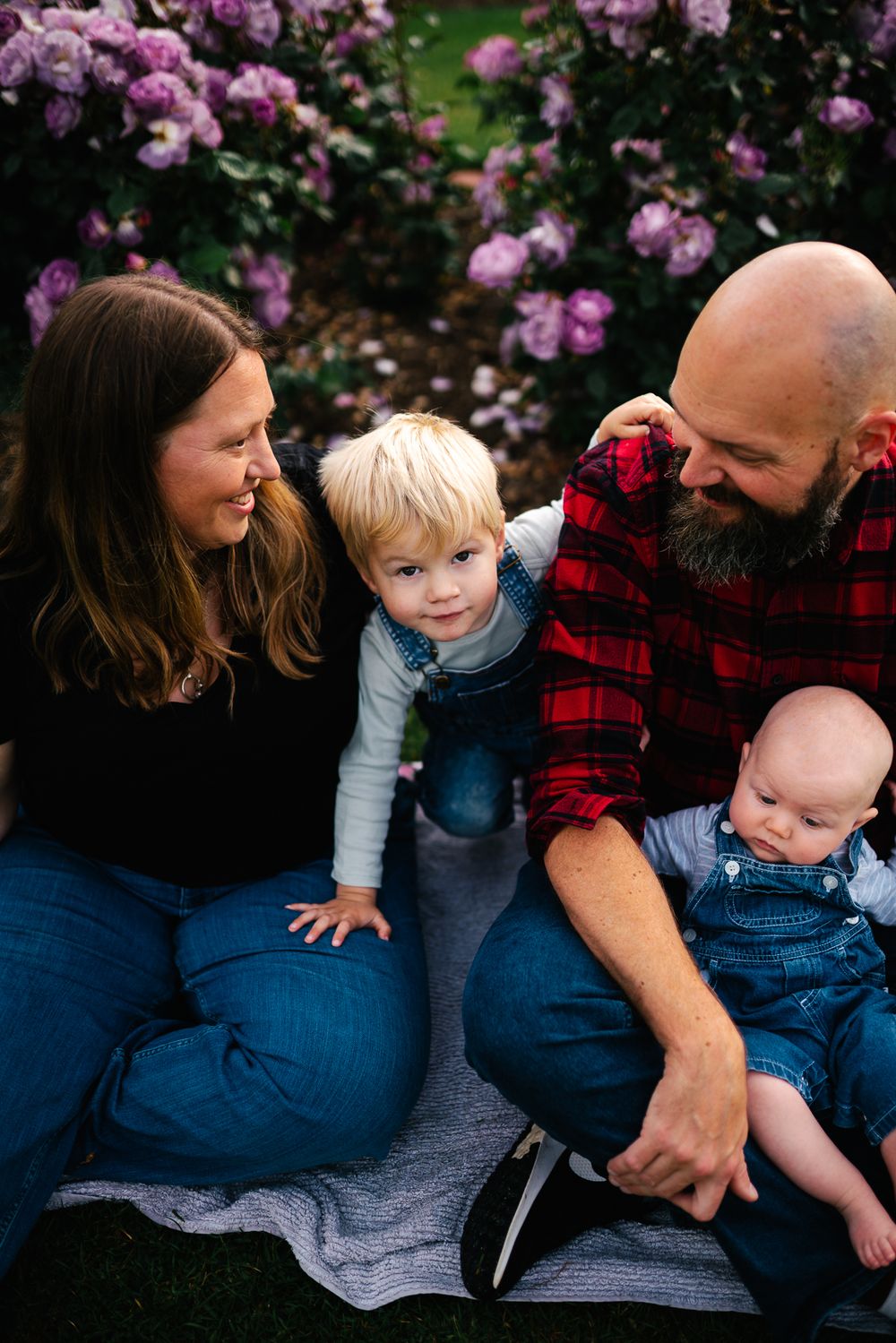 Family sits on blanket together by blooming purple flowers in garden on spring day taken by a Melbourne family photographer