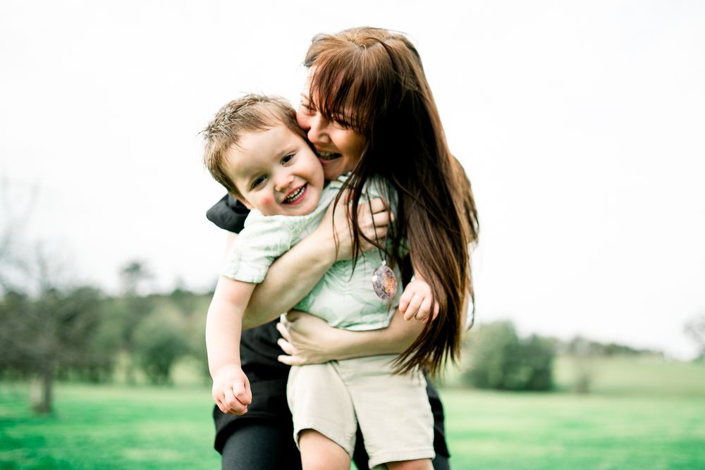An affectionate moment shared between mother and child outdoors in a green field on a sunny day taken by Melbourne family photographer