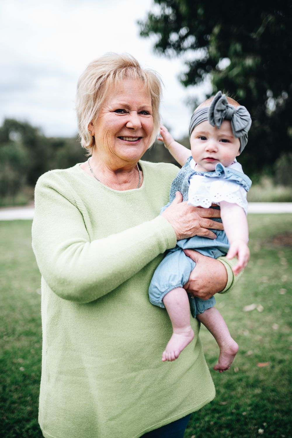 Grandmother in a lime green sweater holding a baby wearing a gray bow headband taken by Melbourne family photographer.