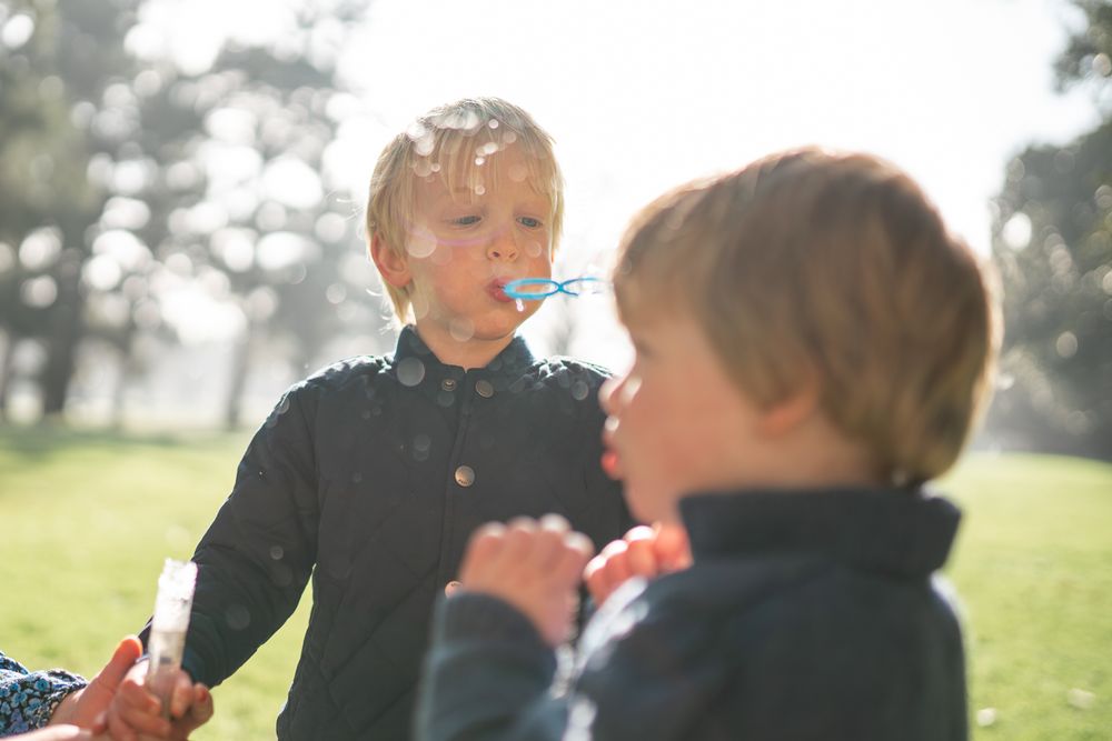 Two young children blowing bubbles together in a sunny park with backlit golden light taken by a Melbourne family photographer.