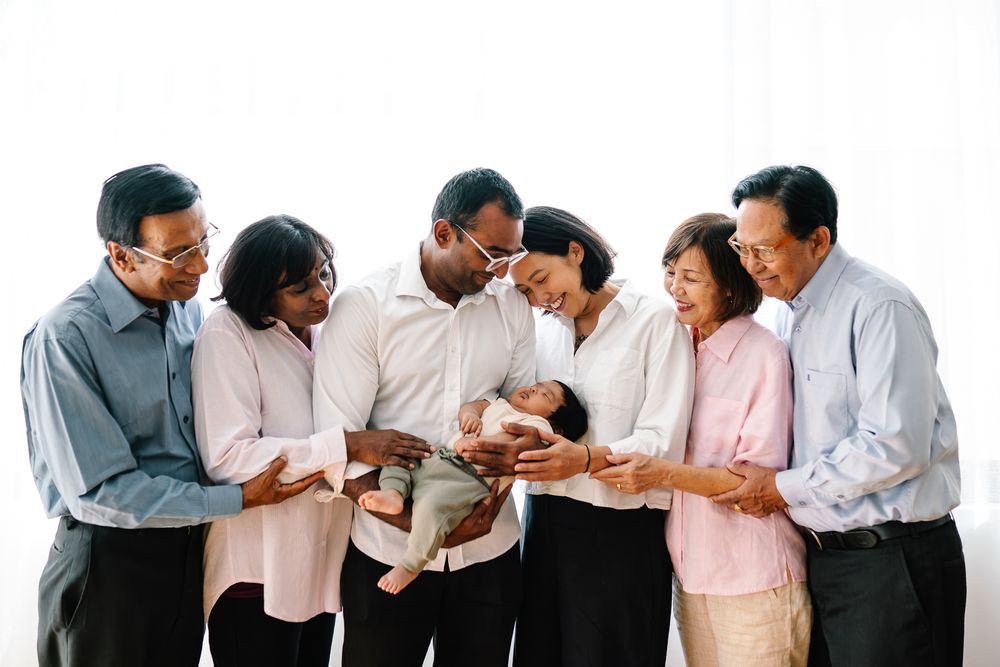 Multigenerational family gathering together admiring a newborn baby, smiling and bonding in a bright indoor setting.