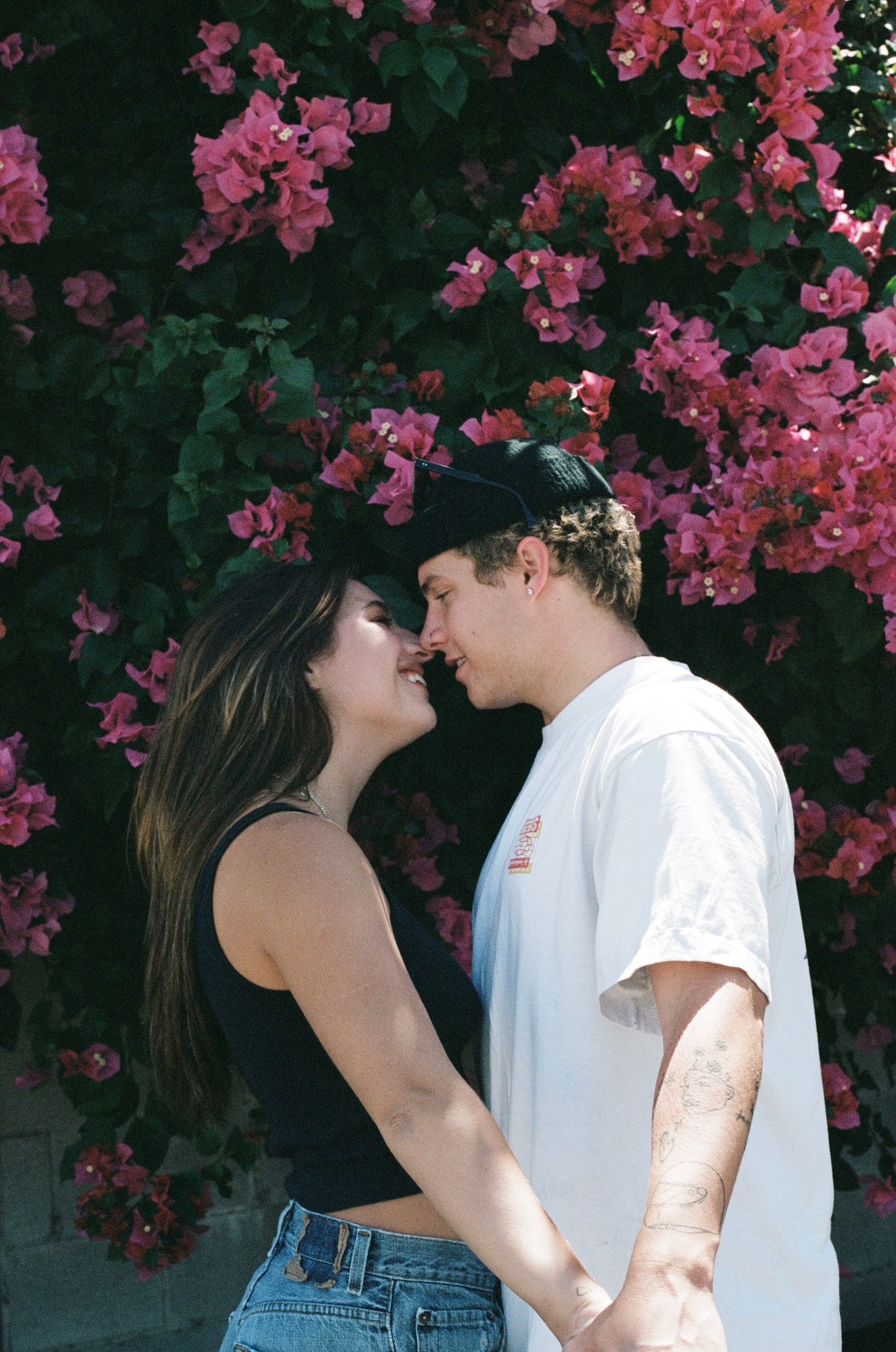 Couple sharing intimate moment against pink flowering bush background.