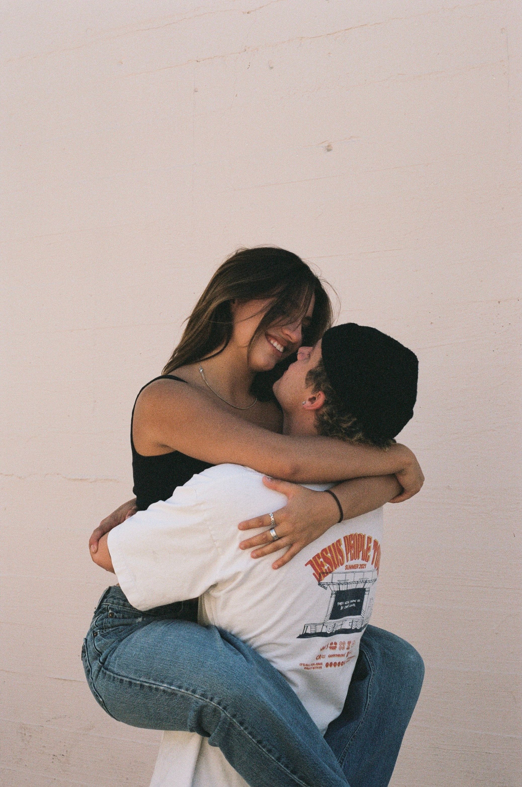 Intimate embrace captured against neutral wall in casual denim outfits.