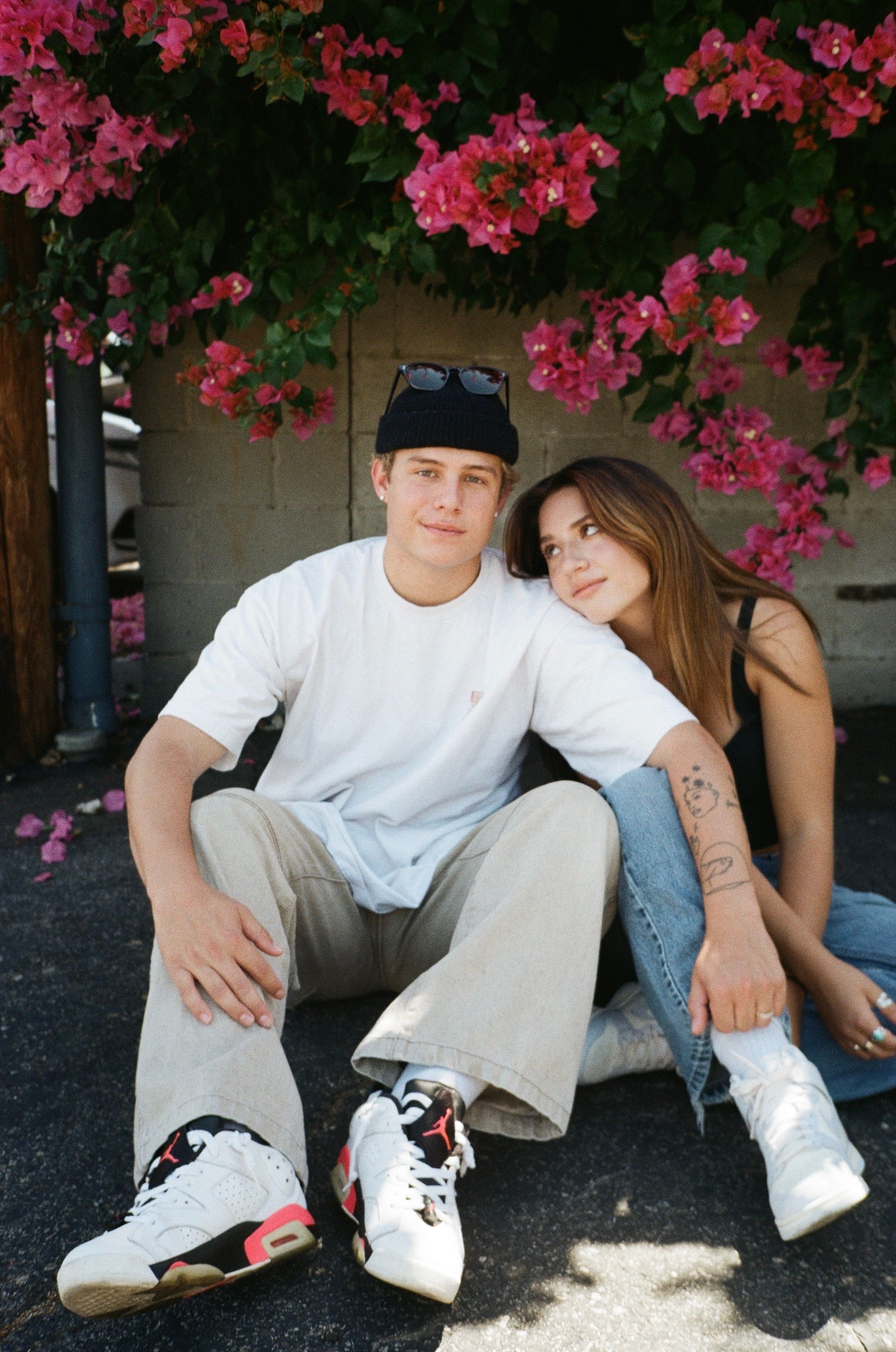 Couple sitting under flowering bougainvillea tree in casual streetwear.