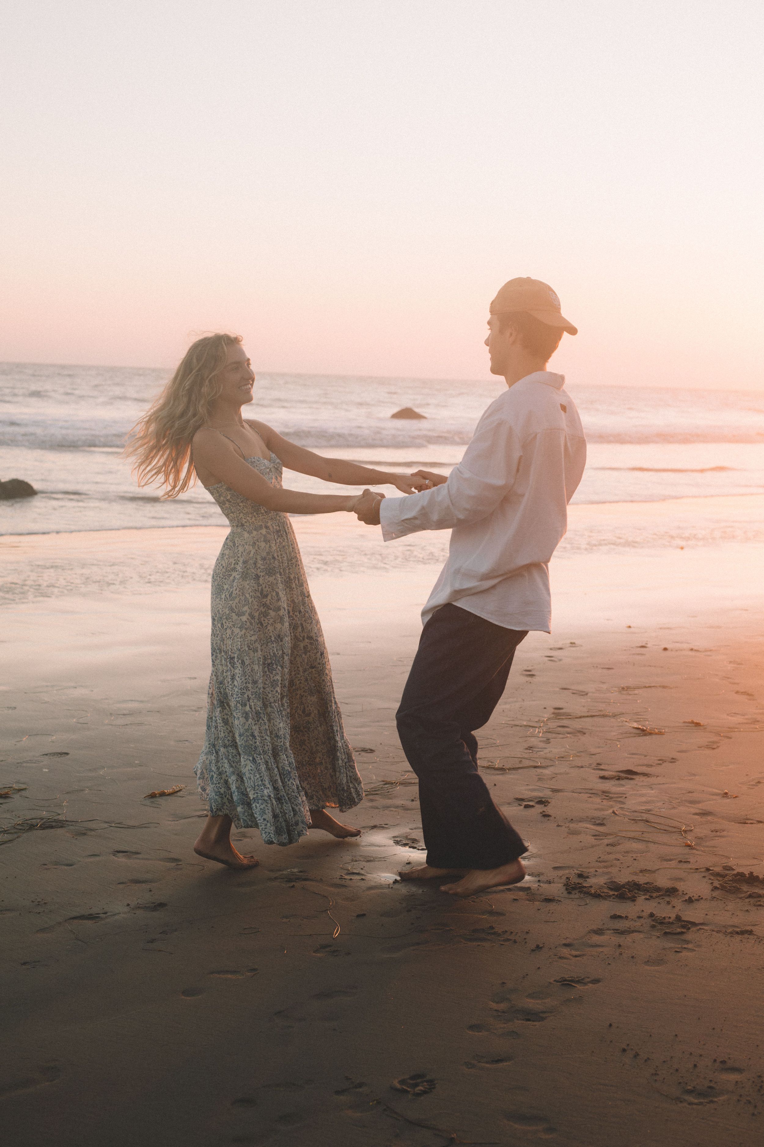 Couple dancing together on sandy beach during sunset.