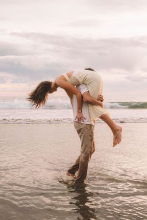 A romantic couple playing in the ocean waves, with one person lifting the other in a playful dip.