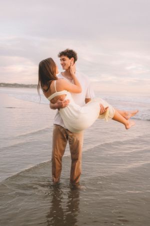A couple sharing a romantic moment in the shallow ocean water during sunset, with one person being carried.