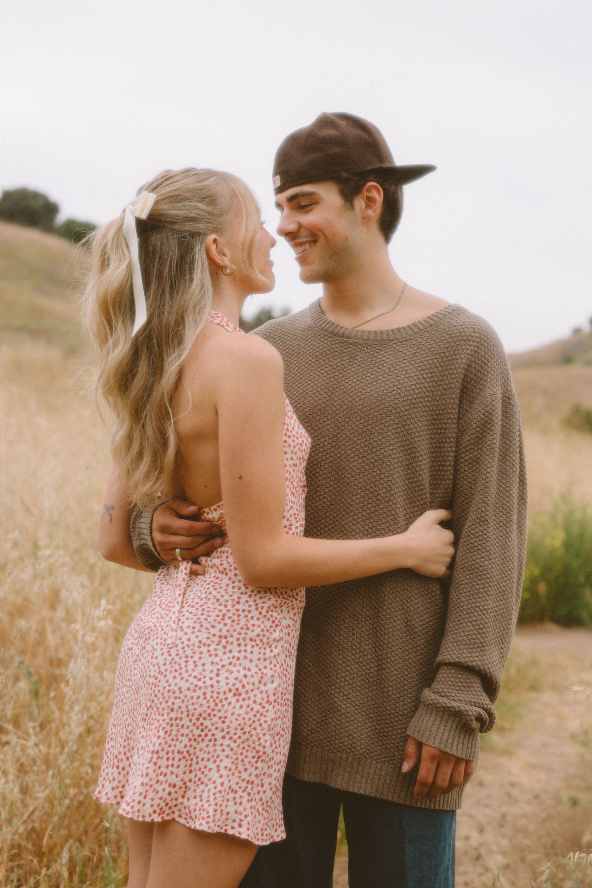 Couple embracing in golden field wearing casual autumn clothing.