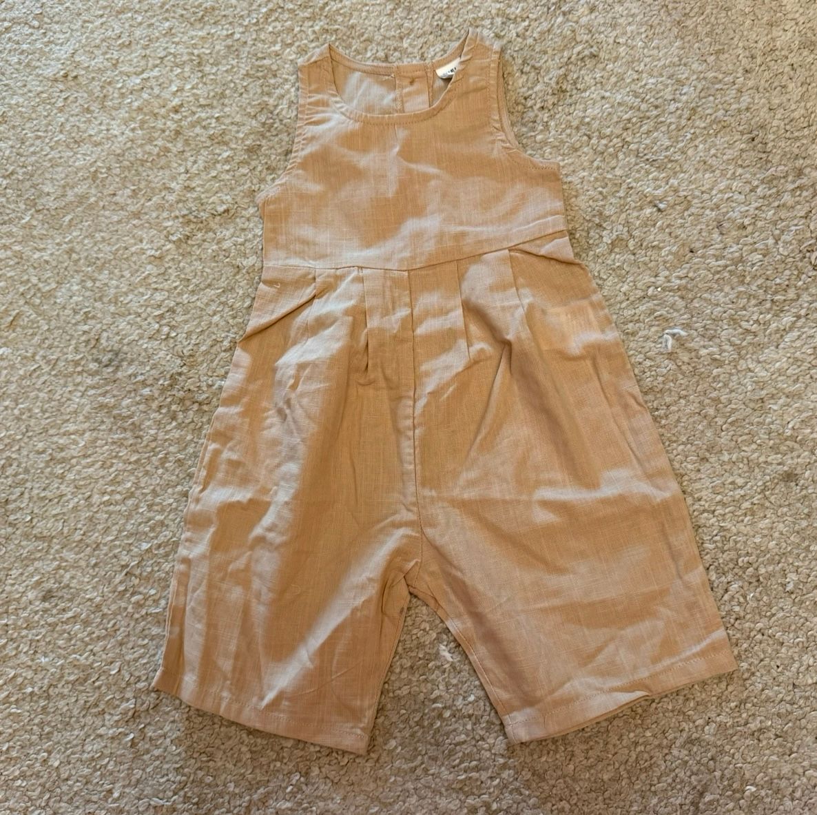 Khaki colored baby shorts displayed on beige carpet.