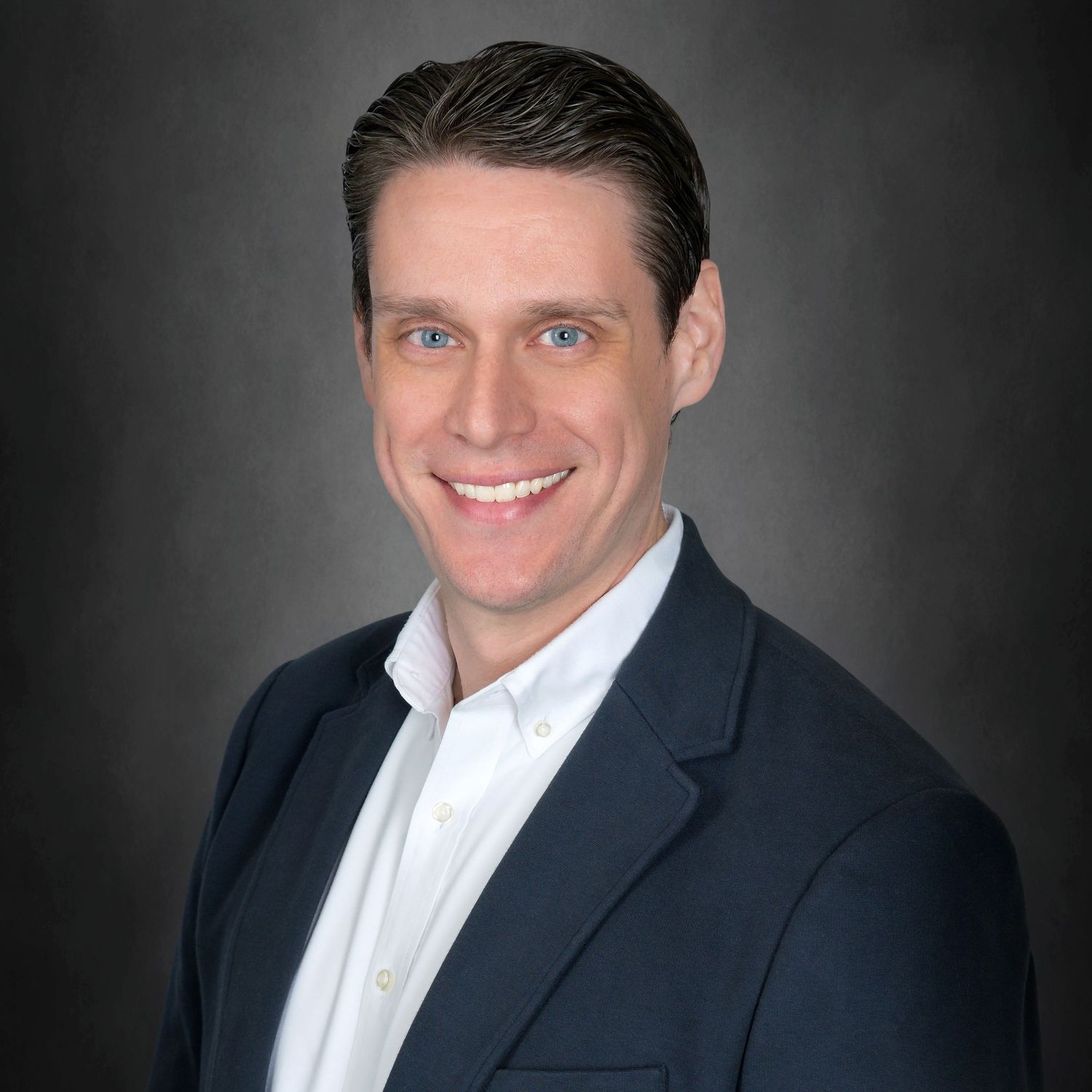 Professional headshot of a person in a navy suit and white dress shirt against a dark gray background.