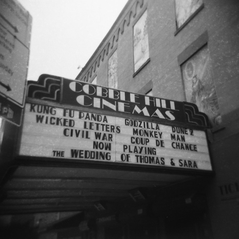 Black and white photo of Cobble Hill Cinemas marquee showing Kung Fu Panda, Godzilla, Civil War, and other films.