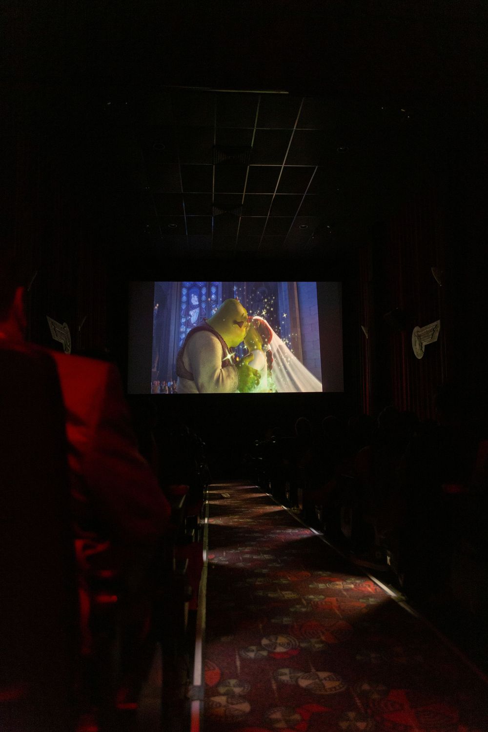 Dark movie theater showing a Shrek with scattered audience silhouettes.