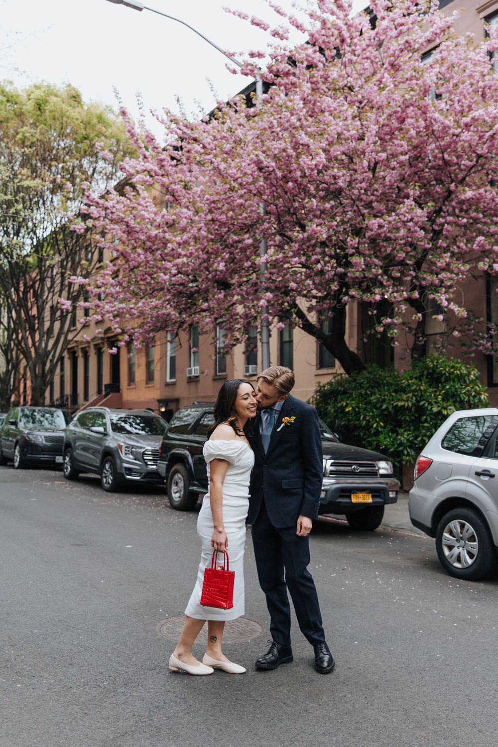 Couple posing under blooming cherry blossom trees on Brooklyn street.