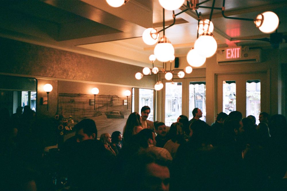 Crowded restaurant event with warm globe pendant lights and guests socializing in a dimly lit dining room.