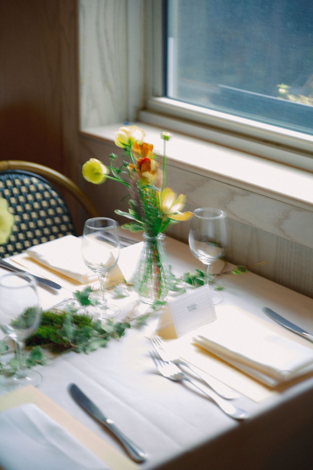 Elegant table setting with small floral centerpieces and place settings near a bright window.
