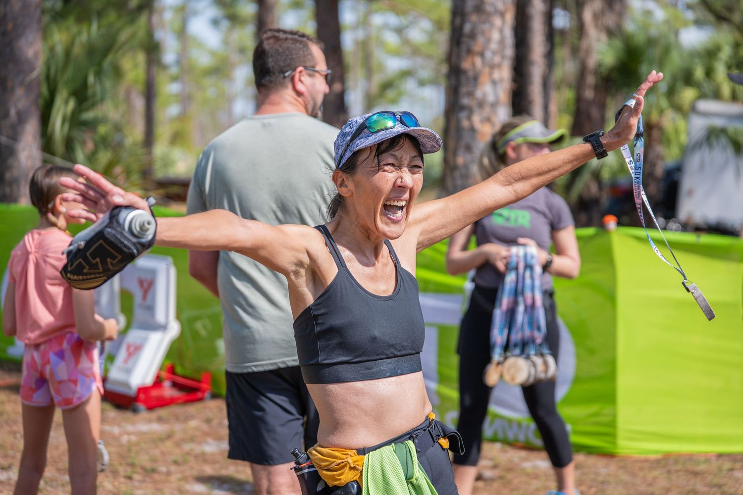 Athlete celebrating with excitement at an outdoor fitness event while others exercise in the background.