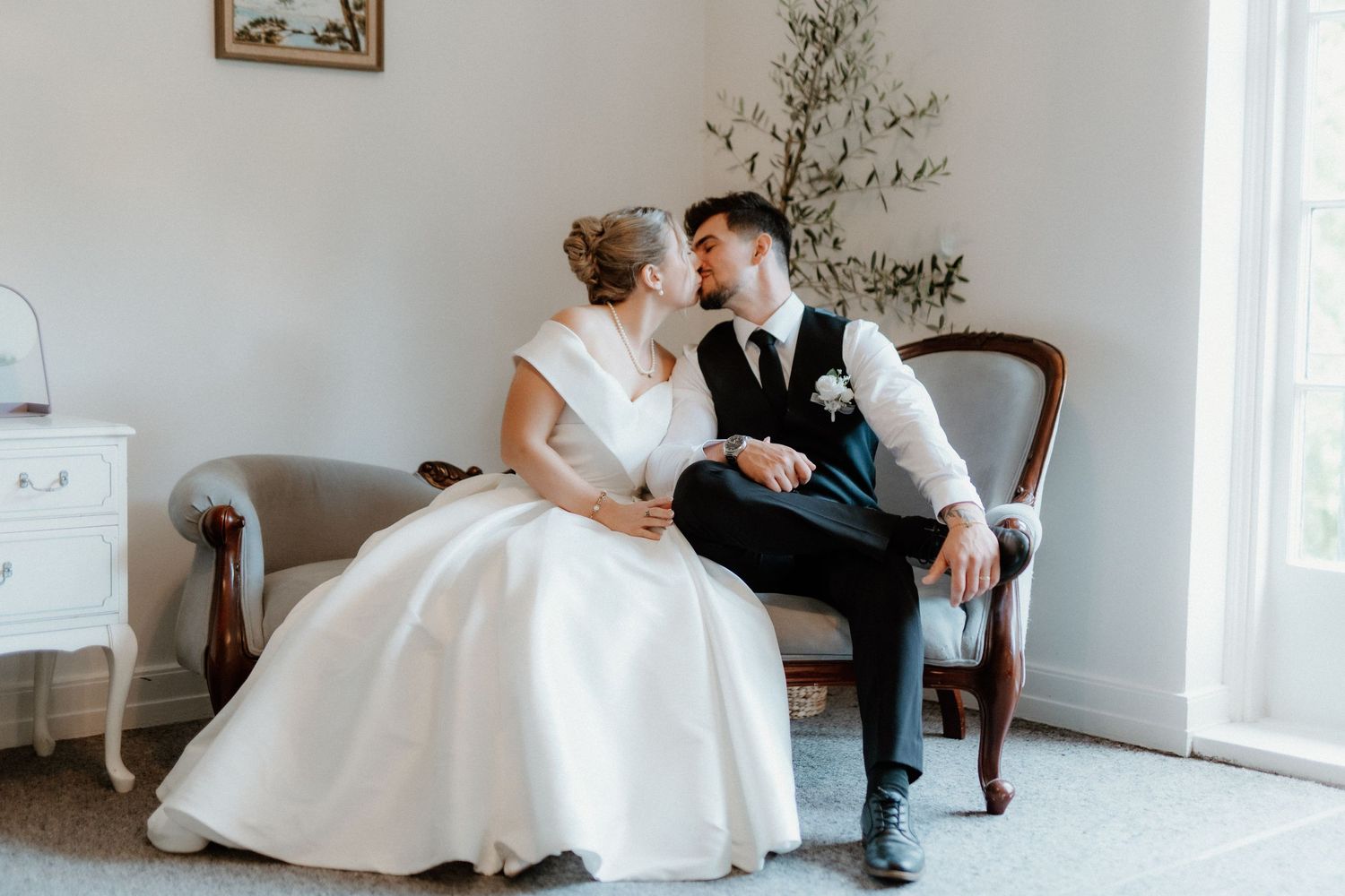 A couple shares an intimate moment while seated on an antique sofa in an elegant white room.